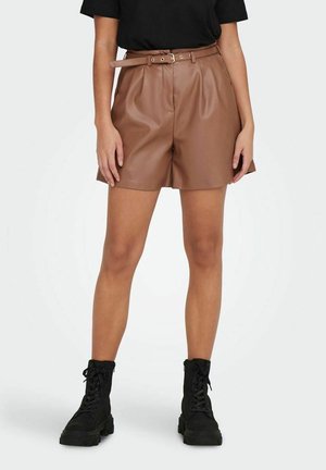 Shorts en simili cuir marron avec une large ceinture, présentant une coupe décontractée et des poches latérales, associés à des bottines noires à lacets.