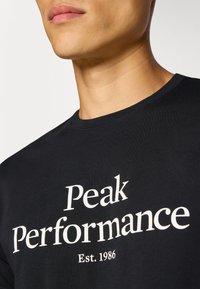 Sort bomulds T-shirt med "Peak Performance" logo i hvid tekst, rund halsudskæring og korte ærmer.