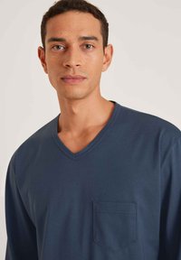 Marineblauwe langwerpige shirt met een V-hals en een borstzak; gemaakt van zachte stof met een gladde textuur. Eenvoudig, minimalistisch ontwerp.