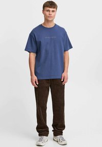 Blaues Baumwoll-T-Shirt mit kurzen Ärmeln und Rundhalsausschnitt, mit gesticktem Text "SPIEL MIR EINE ERINNERUNG." Kombiniert mit braunen Kordhosen.