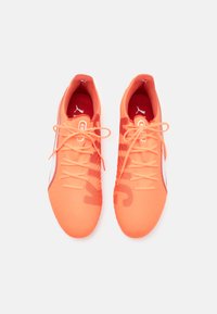 Scarpe da ginnastica di un brillante arancione con una finitura testurizzata, lacci sottili e una fodera interna rossa. Presentano un logo bianco e un motivo sottile sui lati.