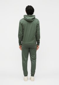 Groene hoodie en bijpassende joggingbroek gemaakt van een zachte katoenmix. Voorzien van een capuchon, aansluitende boorden en details bij de enkels. Eenvoudig, minimalistisch ontwerp.