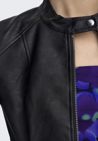 Giacca in pelle sintetica nera con colletto alto, caratterizzata da una chiusura a scatto metallica e una zip frontale. Il tessuto ha un aspetto liscio e leggermente texture.