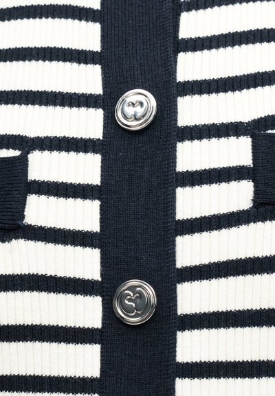 Gros plan sur un tissu en tricot à rayures bleu marine et blanches avec deux boutons décoratifs argentés sur une patte verticale bleu marine.