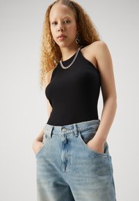 Melnas ribota tank top ar gaiši ziliem augstās jostasvietas platām biksēm. Modelim ir cirtaini mati un sudraba ķēde un apli auskari.
