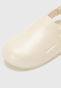 Kremkrāsas, gluds plastikāta klogs ar slēgtu pirkstu, regulējamu siksniņu un teksturētu zoli. Sānos ir nemanāms logs.
