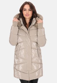 Világos bézs színű, bélelt parka dzseki fényes felülettel, szőrmebéléssel ellátott kapucnival, bordázott mandzsettákkal, cipzáras zsebekkel és enyhén keskenyedő sziluettel.