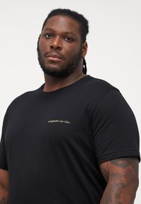 Sort bomulds t-shirt med korte ærmer, prydet med et lille guld-logo på brystet, rund halsudskæring og en glat tekstur.