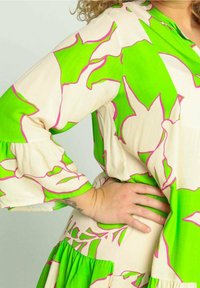 Bloemenjurk met een mix van witte, levendige groene en roze kleuren, met een ontwerp van gerimpelde mouwen en een rok met meerdere lagen.