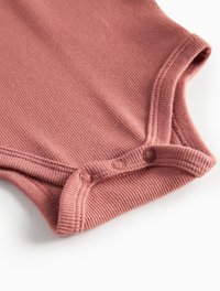 Rippstrick-Bodysuit in staubrosa, mit kurzen Ärmeln und rundem Ausschnitt. Drei Druckknöpfe am Boden für ein einfaches Ankleiden. Weiche Textur.