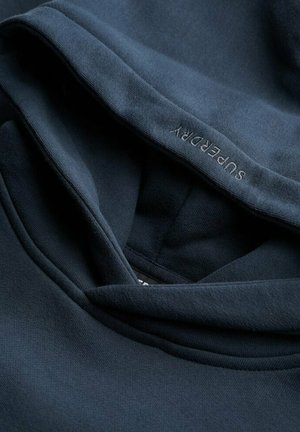 Dark blue hoodie with a soft fabric texture and a relaxed hood. The brand name "Superdry" is subtly embroidered on the inner seam.