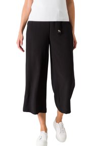 Zwarte, wijde cropped broeken van soepel stof met een trekkoord in de taille. Gecombineerd met witte sneakers voor een casual look.