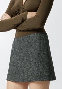 Top lungo marrone a maniche lunghe abbinato a una mini gonna grigia con texture, caratterizzata da un motivo sottile e un design strutturato, mostrato dalla vita in giù.