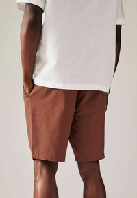 Shorts en coton marron avec une coupe droite et des poches latérales, associés à un t-shirt en lin blanc. Présente un design simple et des couleurs unies.