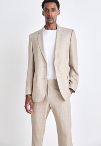 Beige Leinenanzug mit einem strukturierten Blazer, der über zwei Knöpfe verfügt, und passenden Hosen. Kombiniert mit einem weißen T-Shirt, glatter Textur, moderner Schnitt.