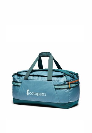 Bolsa de viaje Cotopaxi azul claro y verde azulado con cremallera, dos asas grises y bolsillo lateral con cremallera sobre fondo blanco.