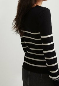 Schwarzer, gerippter Pullover mit weißen horizontalen Streifen, ausgestattet mit langen Ärmeln und einem runden Halsausschnitt, der eine figurbetonte Silhouette präsentiert.