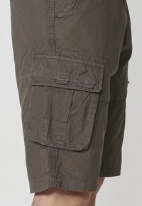 Sötétbarna anyagból készült cargo short, textúrázott mintával, oldalsó zsebekkel és megerősített varrással az alján és a varratok mentén.