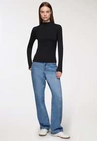 Czarny top z długim rękawem połączony z jasnoniebieskimi szerokimi spodniami dżinsowymi i białymi trampkami, charakteryzujący się dopasowaną sylwetką i minimalistycznym designem.