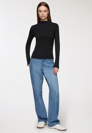 Top nero a maniche lunghe abbinato a jeans a gamba larga blu chiaro e sneakers bianche, con una silhouette aderente e design minimalista.