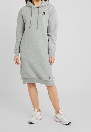 Huppari-mekko harmaasta pehmeästä materiaalista, jossa on kengurutasku, nyörillinen huppu ja logolle omistettu yksityiskohta, yhdistettynä valkoisiin lenkkikenkiin.