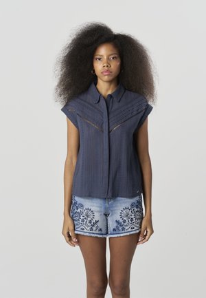 Námornícka košeľa s krátkym rukávom s vertikálnymi pruhmi a vystrihnutými vzormi, v kombinácii s ľahkými džínsovými šortkami s modrou kvetinovou výšivkou.