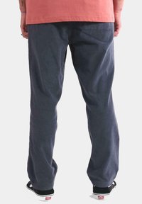Pantalones de pana en azul marino oscuro, con textura acanalada, corte relajado y bolsillos traseros. Combinados con zapatillas negras.