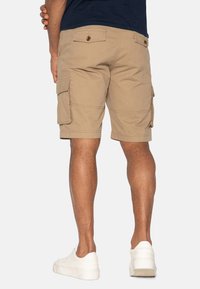 Shorts cargo beiges avec plusieurs poches latérales, un tissu texturé et une coupe décontractée. Associés à des baskets blanches.