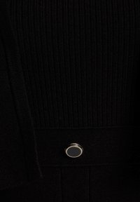 Tela de ribete negra con una textura suave, que presenta un botón plateado redondo con un centro negro, ubicado en la parte inferior.