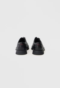 Chaussures en cuir noir avec un dessus texturé, bout rond et semelle en caoutchouc. Présentent un design minimaliste avec de subtils accents rouges.