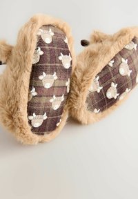 Chaussons moelleux beiges en tissu à carreaux avec de petits motifs de vaches blanches, texture douce, forme arrondie et apparence chaleureuse et confortable.