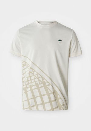 T-shirt blanc à manches courtes avec un motif géométrique beige sur le bas, accompagné d'un petit logo crocodile vert de Lacoste sur la poitrine.