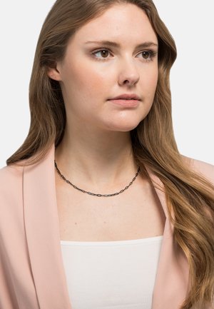 Svart, lenket kjede båret over en hvit topp. Båret med en myk rosa blazer, som har fin tekstur og enkelt, elegant design.