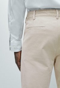 Beige corduroy pants with a straight cut. Features a rear pocket with a horizontal seam. Accompanied by a white long-sleeve shirt.