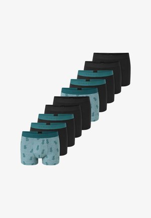 Hombre sin camiseta con cabello rizado, vistiendo calzoncillos bóxer grises con piñas verde oscuro, posando contra un fondo claro y sencillo.