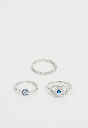 Three silver rings: one with a circular blue stone and small blue accents, one with a textured band, and an eye motif embellished with stones.