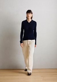Top à manches longues côtelé marine avec col, associé à un pantalon crème ample et des chaussures noires, sur un fond neutre.