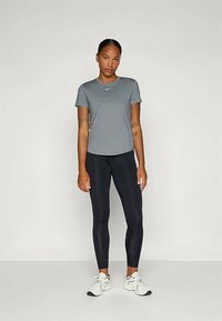 Grå treningstrøye med rund hals, parret med svarte leggings. Modellen har på seg hvite joggesko, som viser en tettsittende og glatt design.