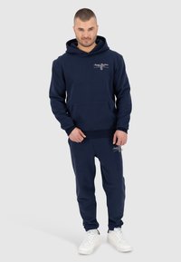Navyblauwe hoodie en bijpassende joggers van zachte stof, met een voorzak en logodetaillering op de borst en het been.