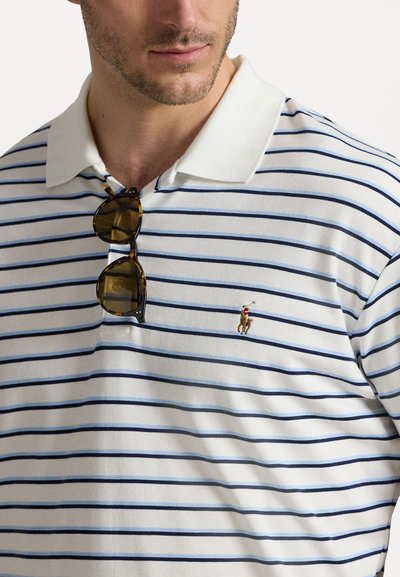 Camisa polo branca com riscas azuis, mangas curtas e colarinho branco sólido. Apresenta um pequeno logo bordado no lado esquerdo do peito.