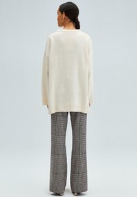 Oversized cream sweater with a ribbed hem, paired with high-waisted, patterned plaid trousers featuring a wide leg and subtle colors.