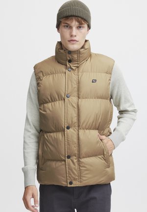 Brown, puffy vest with high collar and front buttons. Features side pockets and a logo on the chest. Worn over a grey long-sleeve shirt.