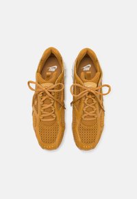 Madala lõikega oranž-pruunid nahast spordijalatsid, millel on võrkpaneelid, ümar nina, paelad ja mustrilised tallad. Nike logo keelele ja küljele.
