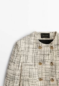 Veste croisée en tissu tissé présentant un motif texturé crème et noir. Boutons dorés et col rond.