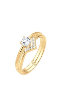 Goldfarbenener Ring mit einem zentralen runden klaren Stein und einem V-förmigen Design, geschmückt mit kleineren klaren Steinen an einer Seite.