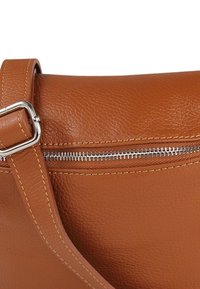 Bruine leren handtas met een gestructureerde afwerking, zilverkleurige ritssluiting en gestikte accenten. Verstelbare riem bevestigd met een metalen gesp.