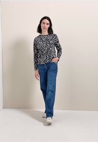 Pitkähihaine paita musta-valkoisessa abstraktissa kuosissa, yhdistettynä sinisiin farkkuihin ja valkoisiin tennareihin, neutraalilla taustalla.