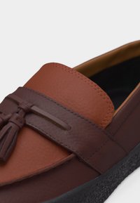 Mocassin en cuir marron avec détail de pampilles, bride marron foncé texturée et semelle noire texturée.