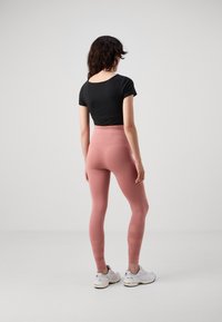 Top nero a maniche corte abbinato a leggings a vita alta in rosa tenue con un motivo testurizzato. La modella indossa sneakers sportive bianche.
