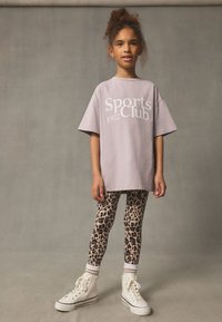 Light purple t-shirt with "Sports Club 1982" printed in white, paired with leopard-print leggings and white high-top sneakers.